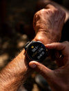Persona usando un reloj deportivo en la muñeca mientras consulta datos de actividad al aire libre, con información de distancia, desnivel y tiempo visible en la pantalla.