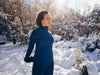Mujer con ropa deportiva azul realizando estiramientos al aire libre en un parque cubierto de nieve, durante un día soleado de invierno