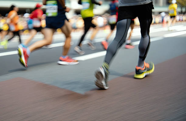 Corredores participando en una carrera de larga distancia por una avenida, con enfoque en sus piernas y tenis deportivos en movimiento.